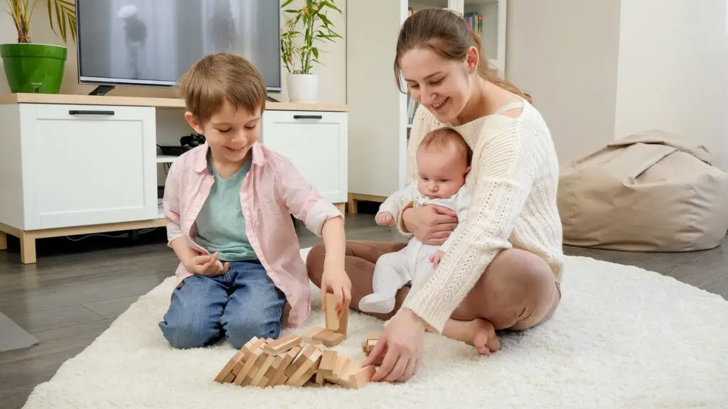 Happy mother with her little sons playing games on floor in living room. Parenting, children